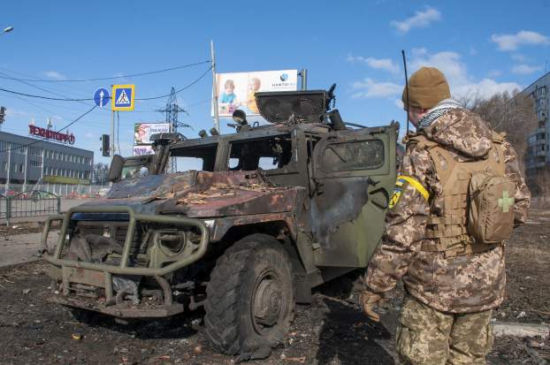 Szétlőtt orosz harcjárművet szemlél egy ukrán katona Harkivban