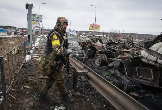 Ukrán fegyveres áll egy orosz harcjármű roncsai mellett a Kijevtől nyugatra levő Bucsa városában