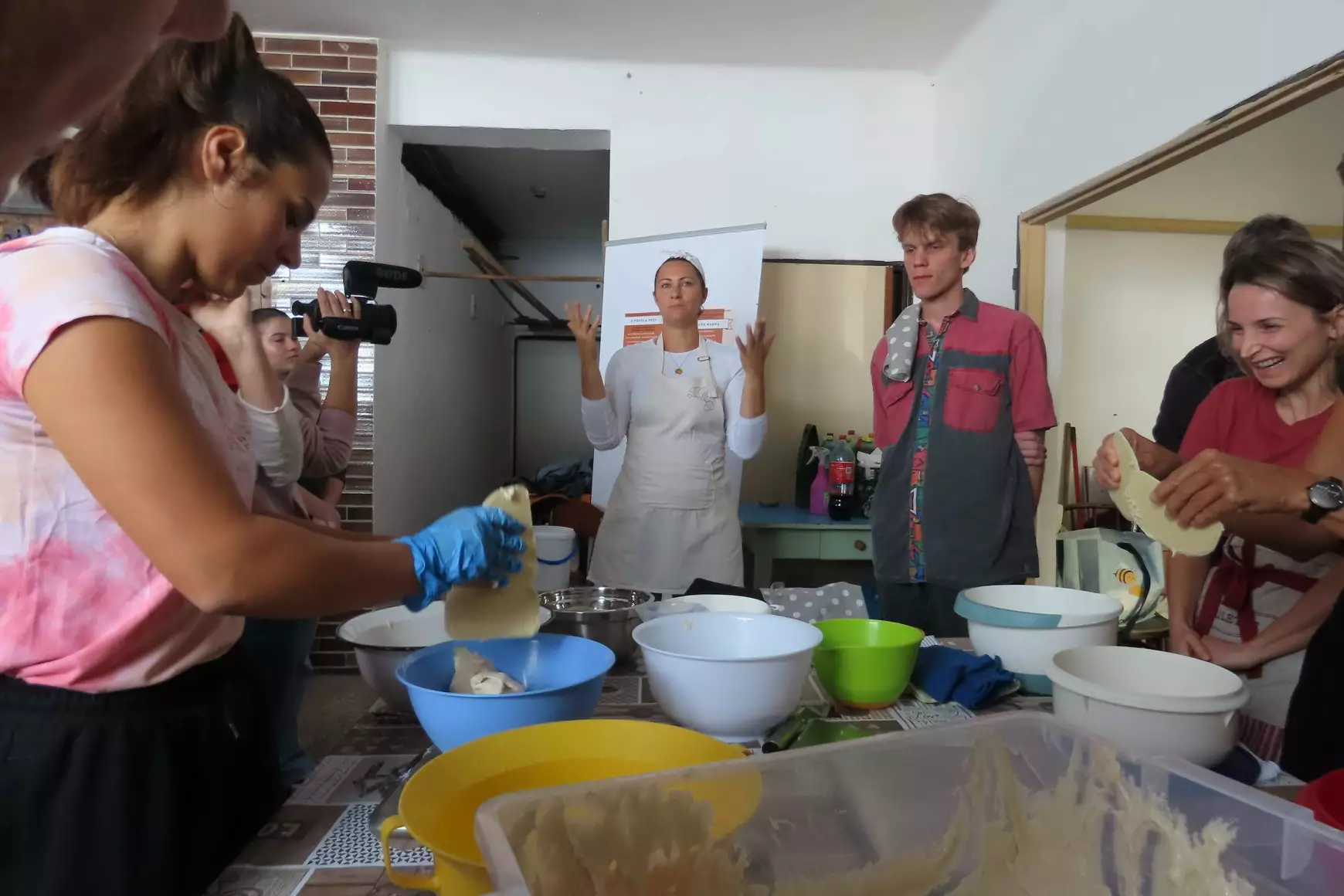 A szőgyéni kenyér mélyen él az emberek emlékezetében, a „szociban” híres volt az egész környéken. Nem csoda, hogy a mostani workshop is sokakat vonzott, Béres Németh Ildikó köbölkúti pékmester vezetésével. Meglepő és örvendetes volt látni, hogy mennyi fiatal lány és fiú is időt szakított arra, hogy a kenyérsütést a gyakorlatban megtanulja. Ildikó irányításával fehér parasztkenyér készült, amelyhez teljes kiőrlésű lisztet is adott, hogy ízesebb legyen. „Minden az alapanyagon múlik” – hangsúlyozta. Ő biogazda